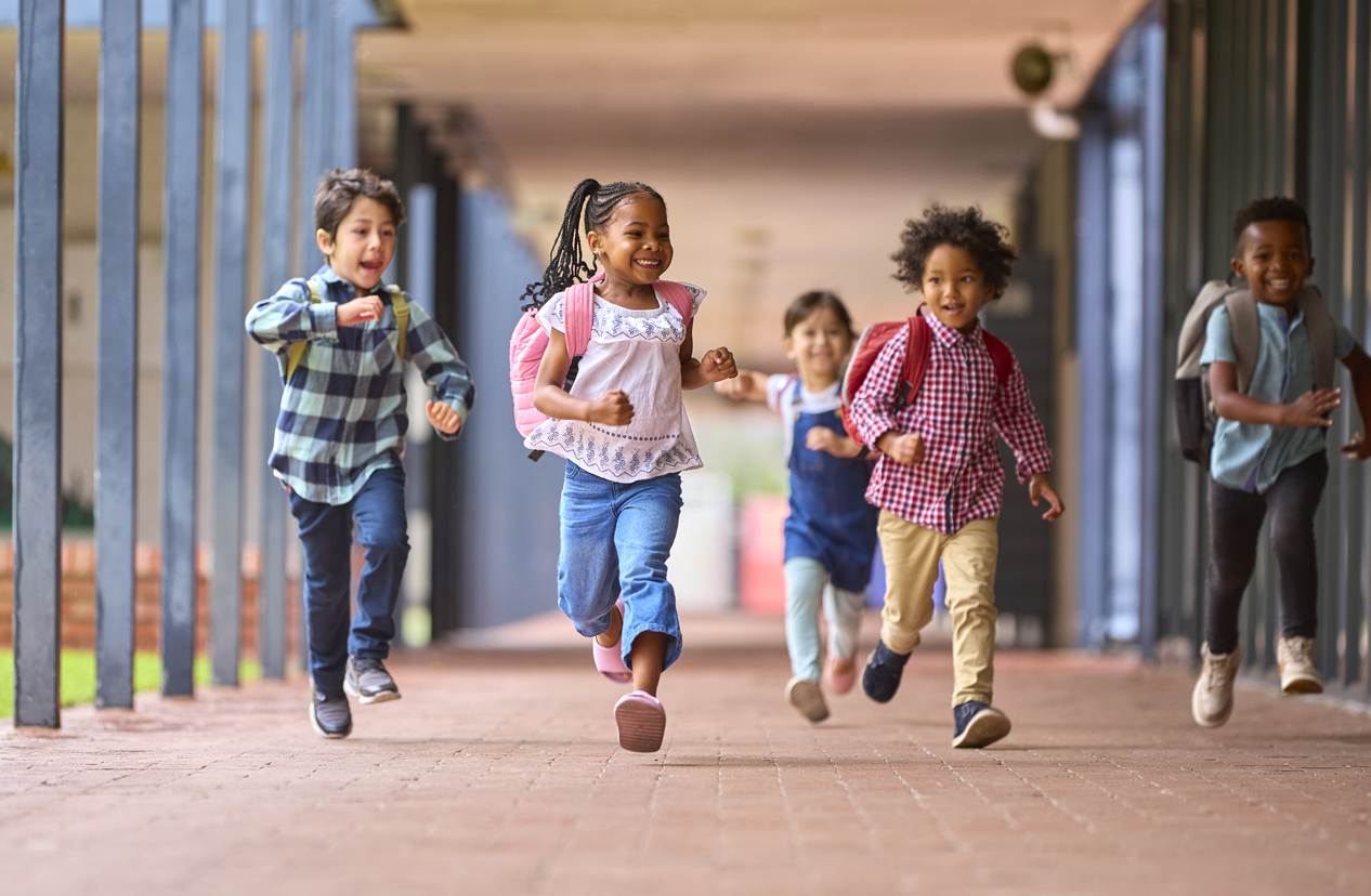 Group Of Multi-Cultural Elementary School Pupils Running Along Walkway Outdoors At School